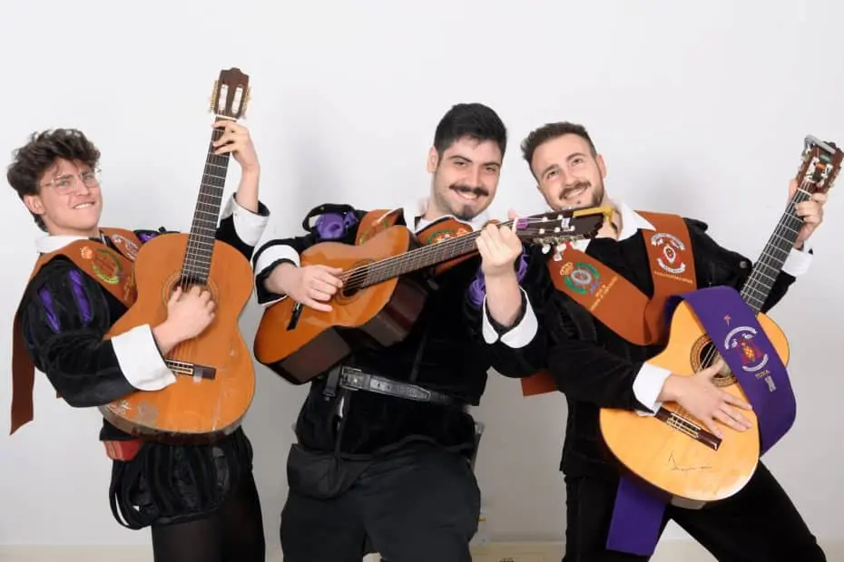 Tres tunos profesionales vestidos con trajes tradicionales y becas, posando con sus guitarras para contratación de eventos en contratartunas.net.